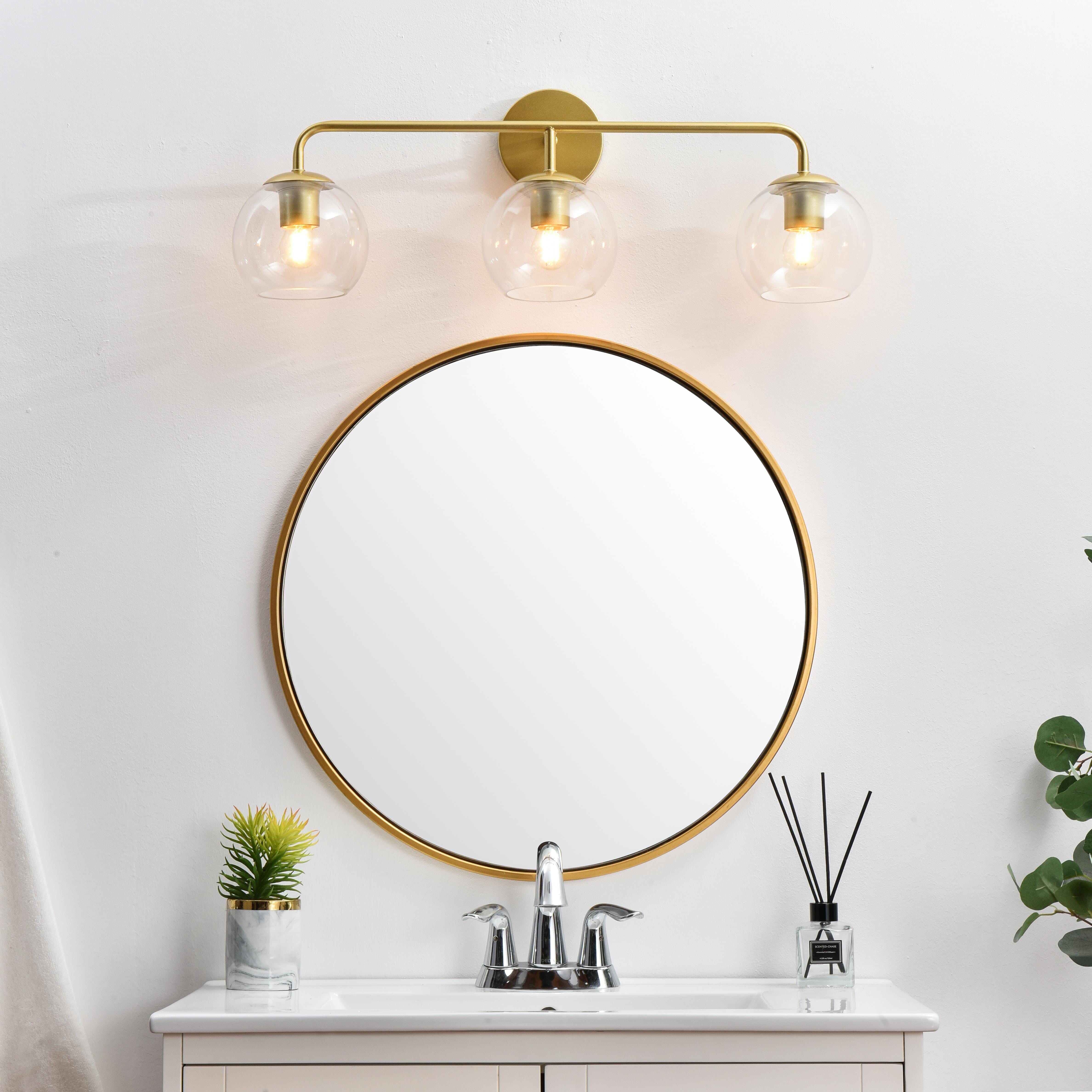 A modern twist on a traditional design, this vanity light is perfect for sprucing up your bathroom. Rated for use in damp locations, this iron fixture features a round backplate, curved arms, and orb accents. Completely versatile, you can place this wall light as an uplight or downlight. Rated for use in damp locations, this will work perfectly over a vanity in your bathroom. Collection: Genesis Rooms: Bathroom Finish: Brass and Clear Glass: Clear Width: 28.00" Height: 10.00" Weight: 3.00 lb Extension from Wall: 8.00" Wire: 8" Black and White Canopy: 4.7"x1"x4.7" Number of Bulbs: 3 Maximum Wattage: 40.00 W Bulb Type: E26 Bulb Base: E26 Dimmable Voltage: 110.00 V Material: Iron and Glass Country of Origin: China Safety Listing: ETL Safety Rating: Damp Title 20 Title 24 Manufacturer Warranty: 1 year limited - alternate view