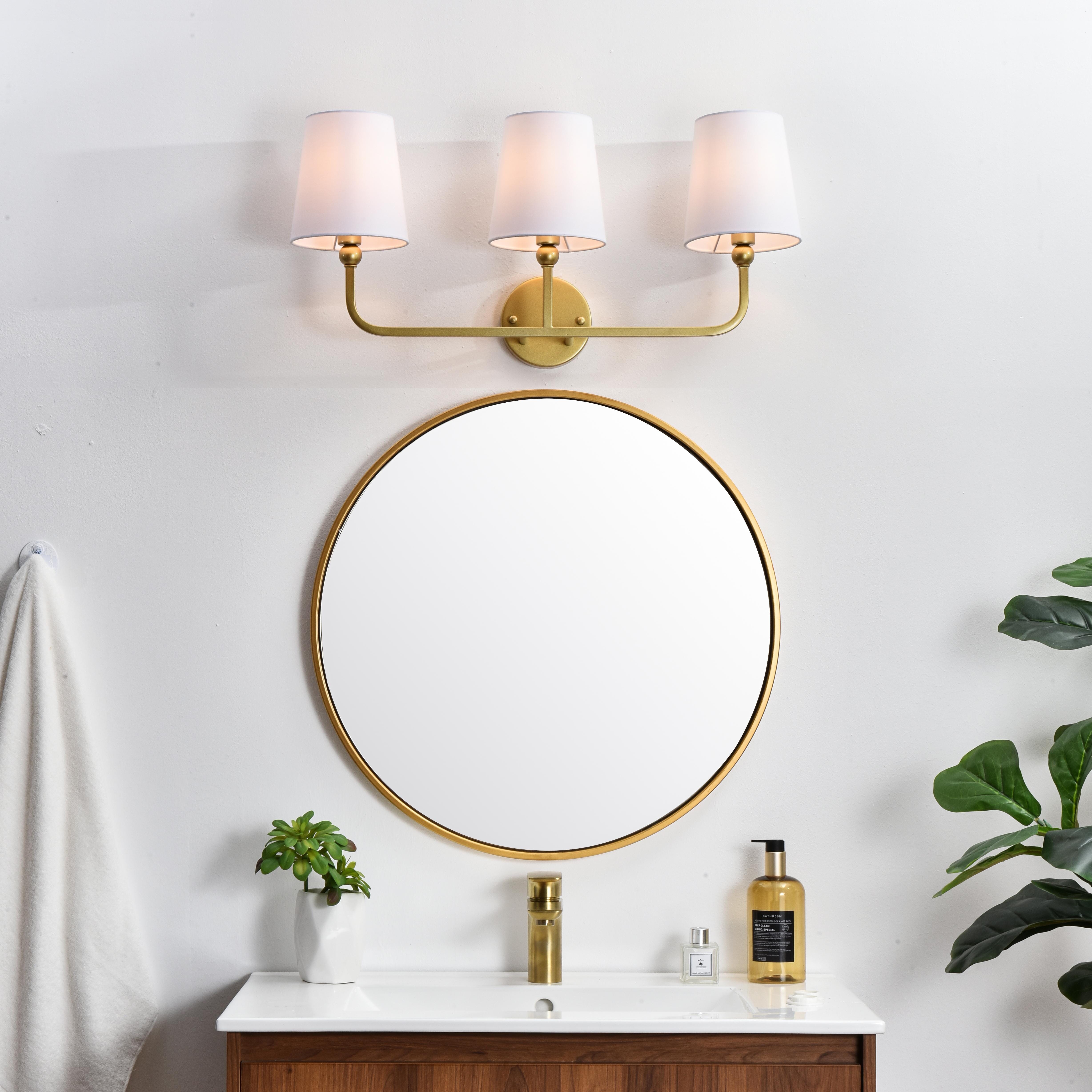 A modern twist on a traditional design, this vanity light is perfect for sprucing up your bathroom. Rated for use in damp locations, this iron fixture features a round backplate, curved arms, and fabric shade accents. Completely versatile, you can place this wall light as an uplight or downlight. Rated for use in damp locations, this will work perfectly over a vanity in your bathroom. Collection: Colson Rooms: Bathroom Finish: Brass and Clear Glass: White Width: 26.00" Height: 12.00" Weight: 3.00 lb Extension from Wall: 7.50" Wire: 8" Black and White Canopy: 4.7"x1"x4.7" Number of Bulbs: 3 Maximum Wattage: 40.00 W Bulb Type: E12 Bulb Base: E12 Dimmable Voltage: 110.00 V Material: Metal and Fabric shade Country of Origin: China Safety Listing: ETL Safety Rating: Damp Title 20 Title 24 Manufacturer Warranty: 1 year limited - alternate view