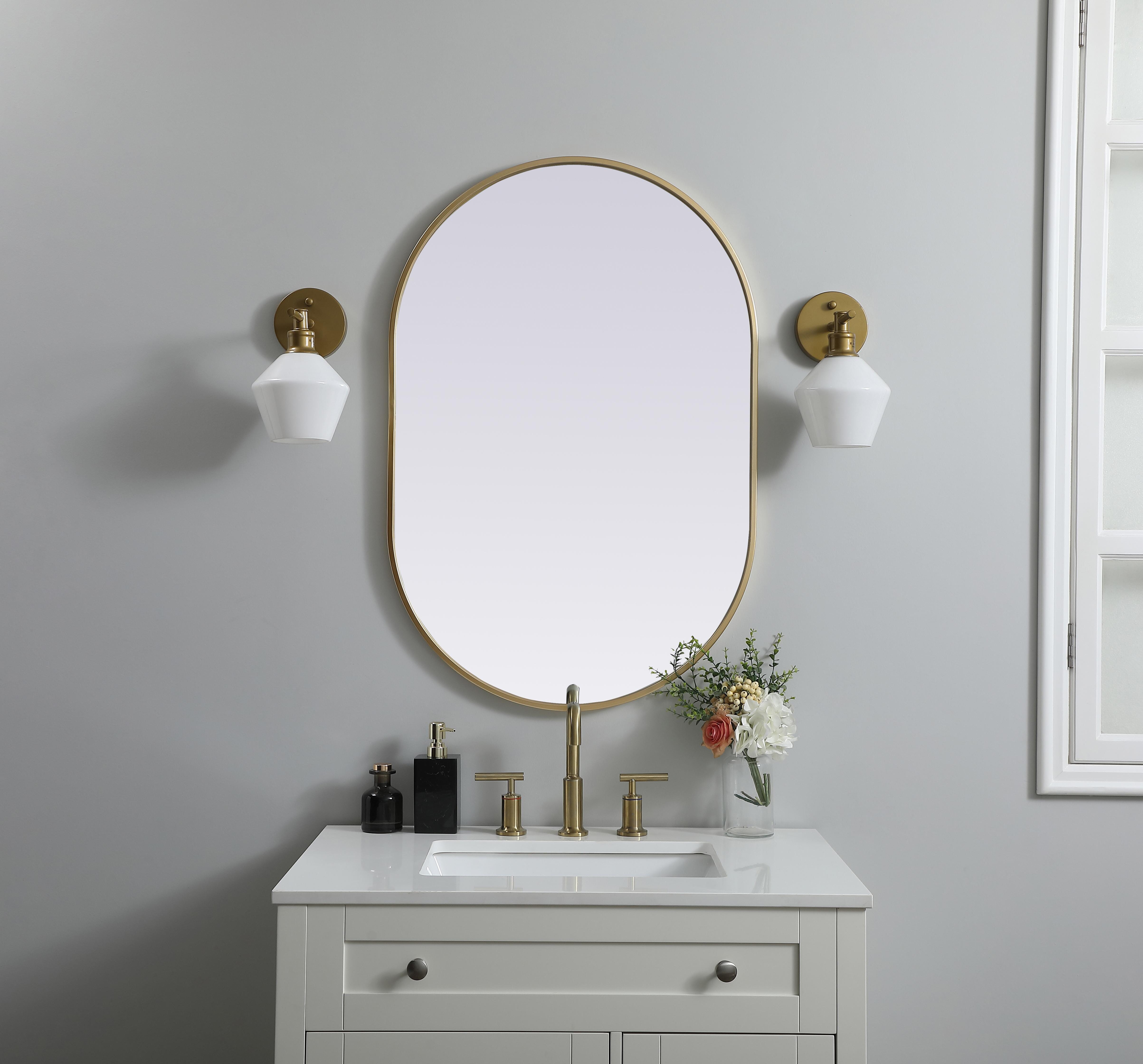 Instantly open up any space in your home with this minimalist wall-mounted mirror. Crafted of metal, this mirror strikes a pill-shaped silhouette. Its slender, clean-lined frame sports a classic finish, while the glass mirror within features a flat, for a brilliant reflection, letting the light bounce off to expand your space. Designed in a pill shape, this metal-frame mirror showcases in the three available satin finishes in black, brass, or silver. Mount this work of art in any room of your choice for added visual impact. Collection: Asha Finish: Brass Width: 24.00" Height: 36.00" Length: 36.00" Weight: 14.00 lb Material: iron and MDF Country of Origin: China Manufacturer Warranty: 1 year limited - alternate view