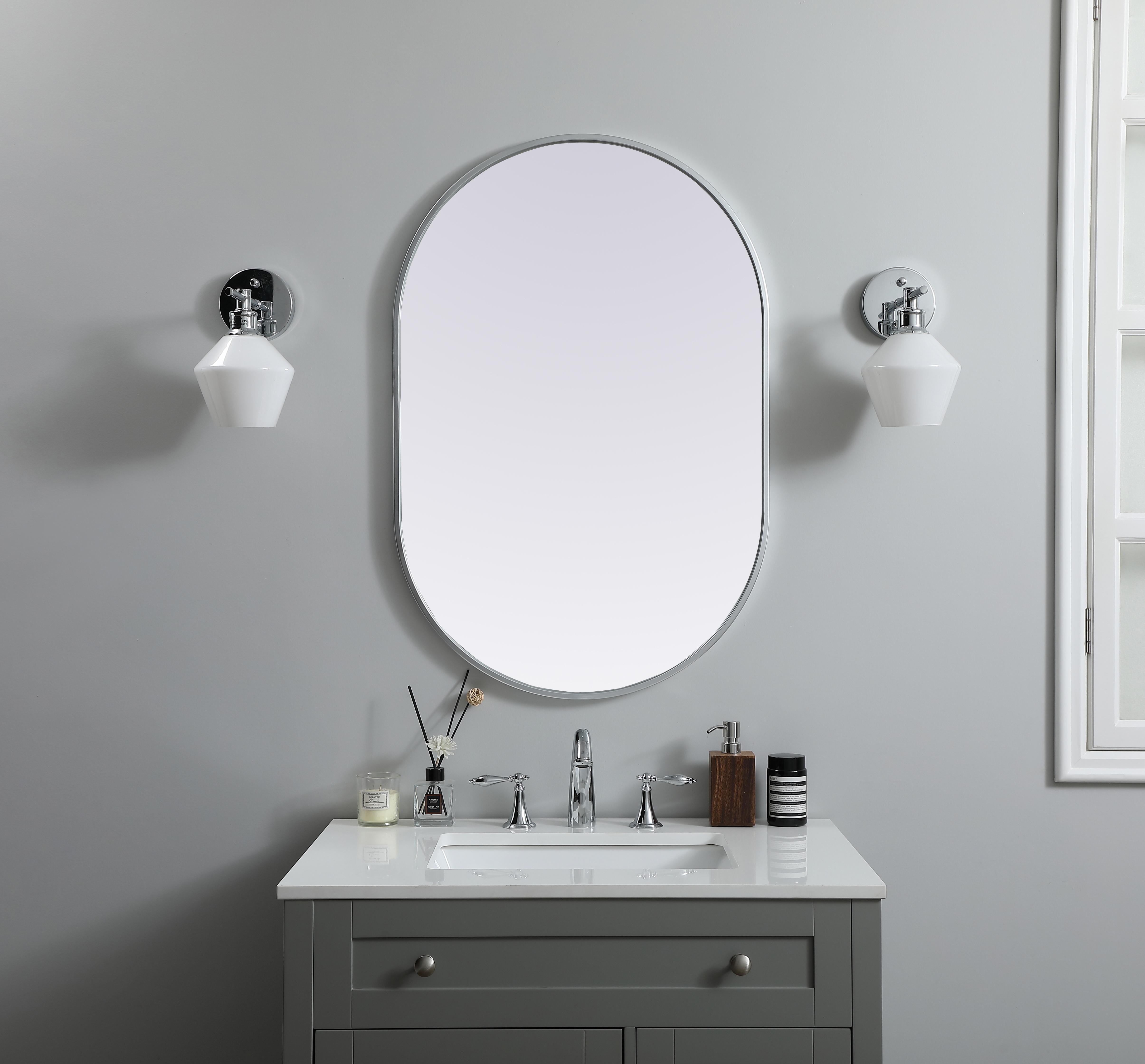 Instantly open up any space in your home with this minimalist wall-mounted mirror. Crafted of metal, this mirror strikes a pill-shaped silhouette. Its slender, clean-lined frame sports a classic finish, while the glass mirror within features a flat, for a brilliant reflection, letting the light bounce off to expand your space. Designed in a pill shape, this metal-frame mirror showcases in the three available satin finishes in black, brass, or silver. Mount this work of art in any room of your choice for added visual impact. Collection: Asha Finish: Silver Width: 24.00" Height: 36.00" Length: 36.00" Weight: 14.00 lb Material: iron and MDF Country of Origin: China Manufacturer Warranty: 1 year limited - alternate view