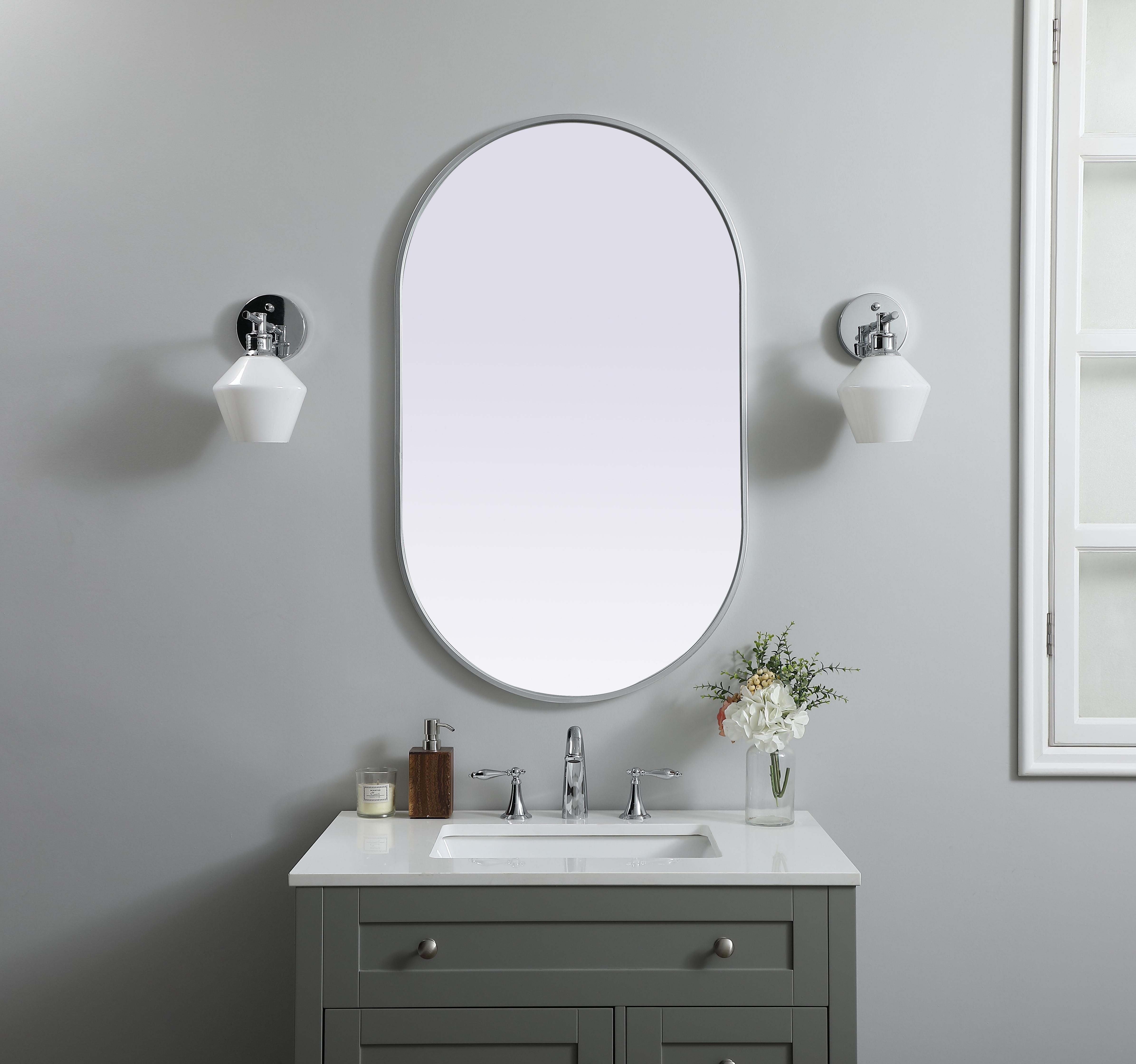 Instantly open up any space in your home with this minimalist wall-mounted mirror. Crafted of metal, this mirror strikes a pill-shaped silhouette. Its slender, clean-lined frame sports a classic finish, while the glass mirror within features a flat, for a brilliant reflection, letting the light bounce off to expand your space. Designed in a pill shape, this metal-frame mirror showcases in the three available satin finishes in black, brass, or silver. Mount this work of art in any room of your choice for added visual impact. Collection: Asha Finish: Silver Width: 24.00" Height: 40.00" Length: 40.00" Weight: 16.00 lb Material: iron and MDF Country of Origin: China Manufacturer Warranty: 1 year limited - alternate view
