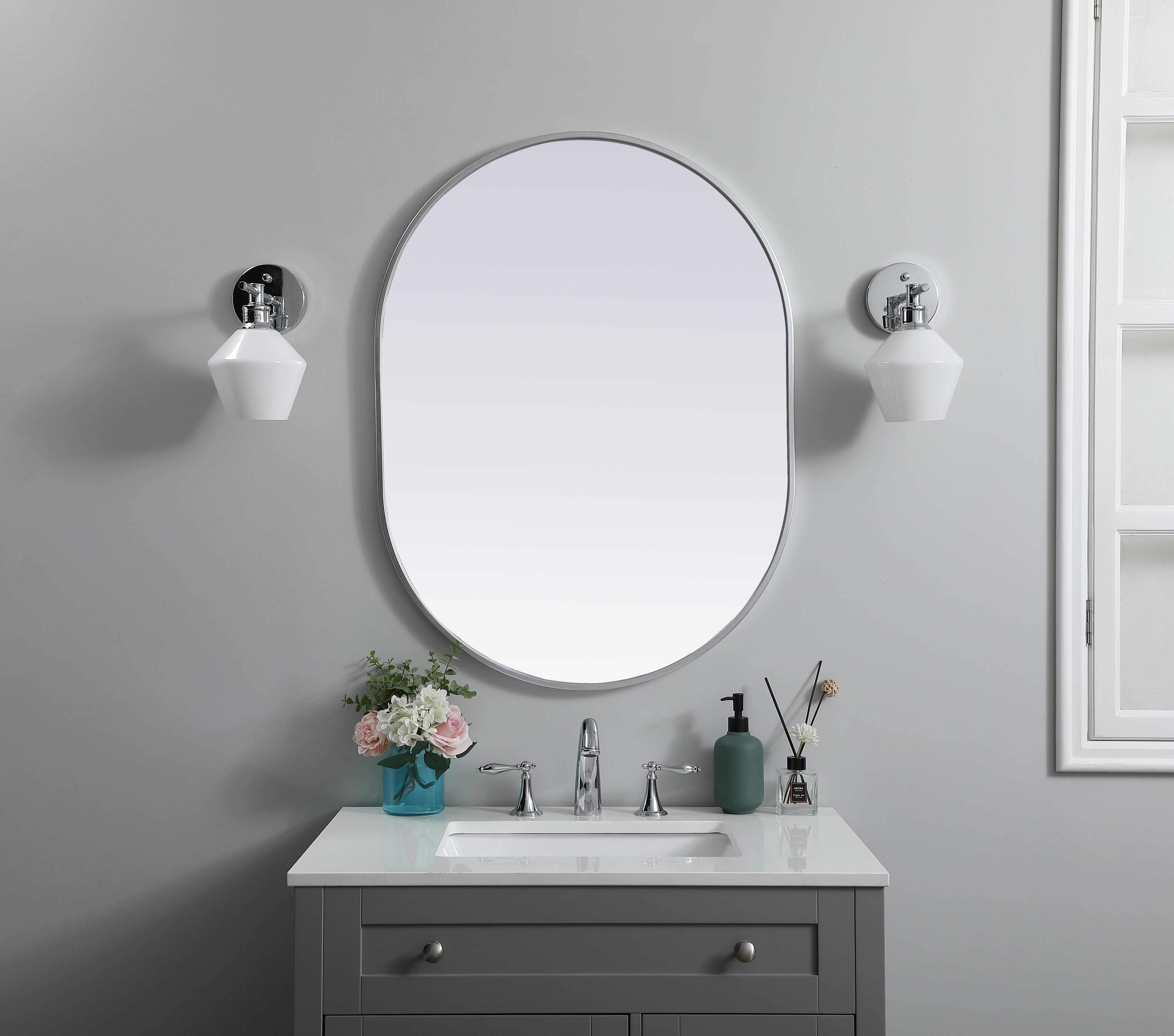 Instantly open up any space in your home with this minimalist wall-mounted mirror. Crafted of metal, this mirror strikes a pill-shaped silhouette. Its slender, clean-lined frame sports a classic finish, while the glass mirror within features a flat, for a brilliant reflection, letting the light bounce off to expand your space. Designed in a pill shape, this metal-frame mirror showcases in the three available satin finishes in black, brass, or silver. Mount this work of art in any room of your choice for added visual impact. Collection: Asha Finish: Silver Width: 27.00" Height: 36.00" Length: 36.00" Weight: 16.00 lb Material: iron and MDF Country of Origin: China Manufacturer Warranty: 1 year limited - alternate view