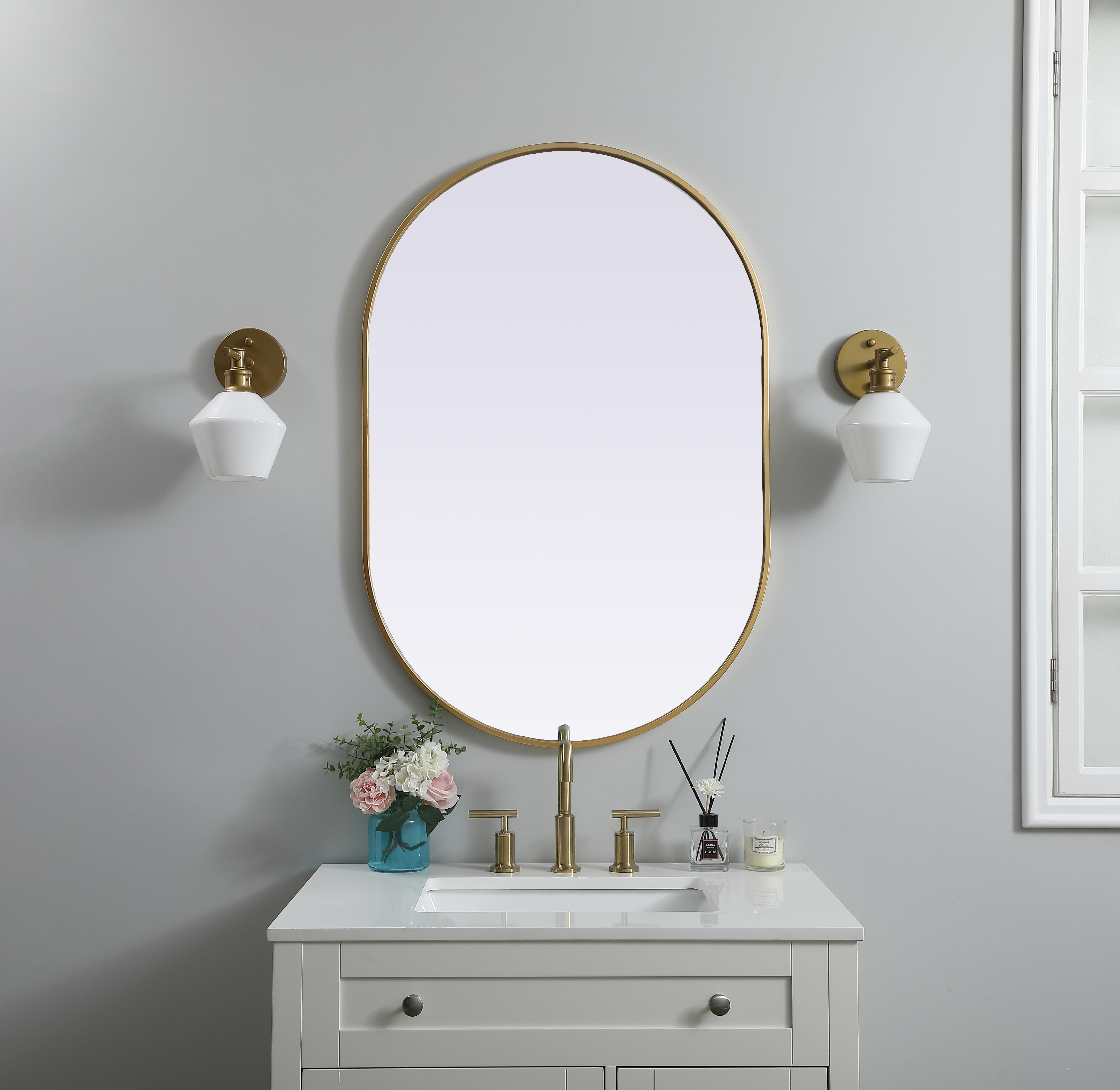 Instantly open up any space in your home with this minimalist wall-mounted mirror. Crafted of metal, this mirror strikes a pill-shaped silhouette. Its slender, clean-lined frame sports a classic finish, while the glass mirror within features a flat, for a brilliant reflection, letting the light bounce off to expand your space. Designed in a pill shape, this metal-frame mirror showcases in the three available satin finishes in black, brass, or silver. Mount this work of art in any room of your choice for added visual impact. Collection: Asha Finish: Brass Width: 27.00" Height: 40.00" Length: 40.00" Weight: 18.00 lb Material: iron and MDF Country of Origin: China Manufacturer Warranty: 1 year limited - alternate view