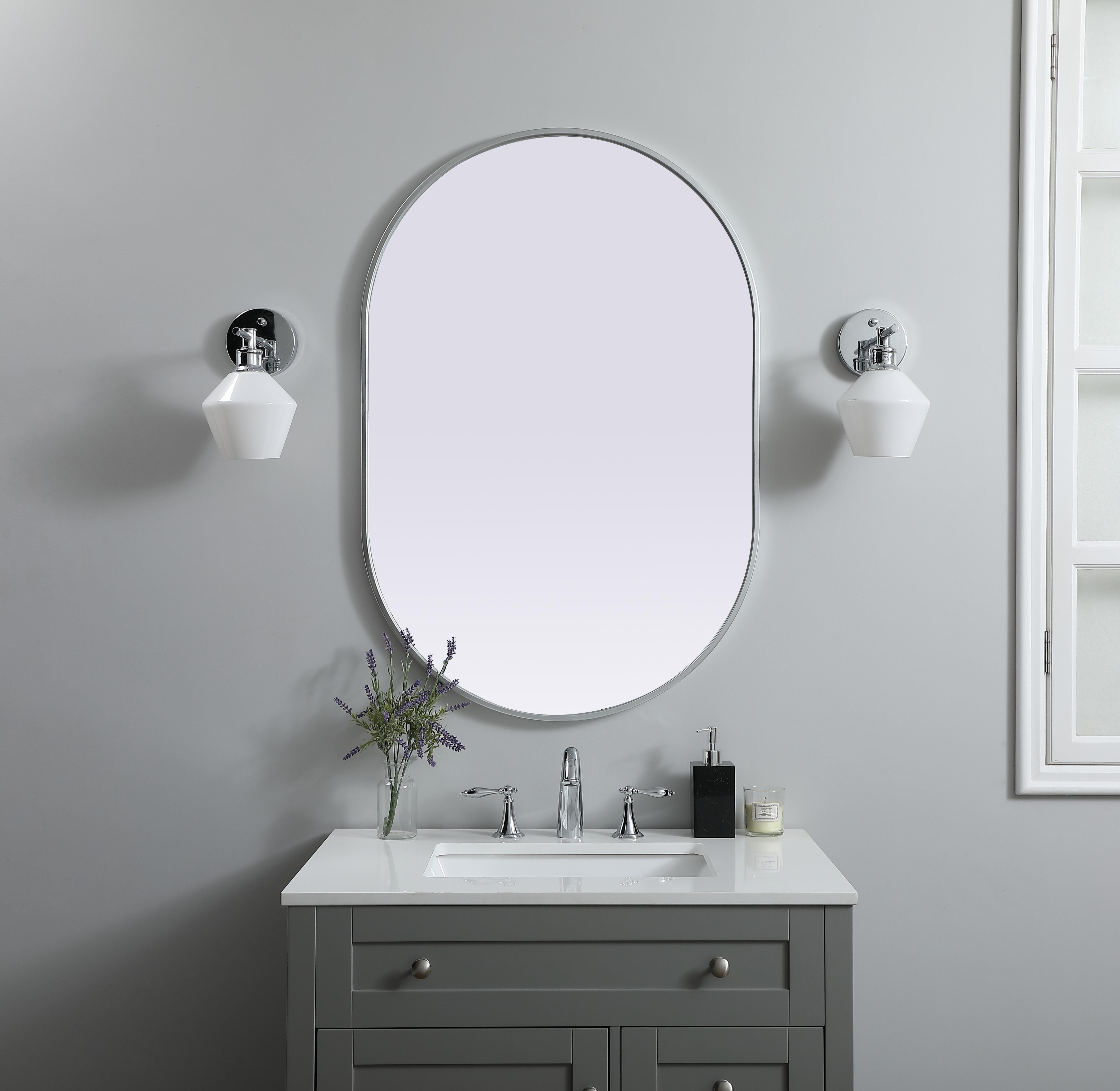 Instantly open up any space in your home with this minimalist wall-mounted mirror. Crafted of metal, this mirror strikes a pill-shaped silhouette. Its slender, clean-lined frame sports a classic finish, while the glass mirror within features a flat, for a brilliant reflection, letting the light bounce off to expand your space. Designed in a pill shape, this metal-frame mirror showcases in the three available satin finishes in black, brass, or silver. Mount this work of art in any room of your choice for added visual impact. Collection: Asha Finish: Silver Width: 27.00" Height: 40.00" Length: 40.00" Weight: 18.00 lb Material: iron and MDF Country of Origin: China Manufacturer Warranty: 1 year limited - alternate view
